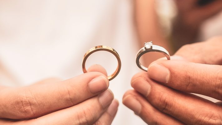 Pria sedang memegang dua buah jenis cincin perak dan cincin emas